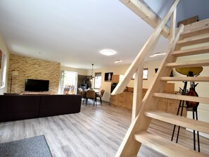 Uma sala de estar moderna com escada de madeira, televisão de tela plana e área de jantar com mobiliário em madeira.