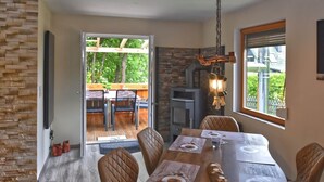 Un comedor con una mesa de madera, sillas con cojines, una pared de acento de piedra, una chimenea y un farol colgante.