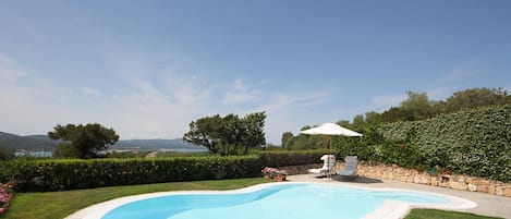 A swimming pool with a white deck, surrounded by a well-maintained lawn and a stone wall.