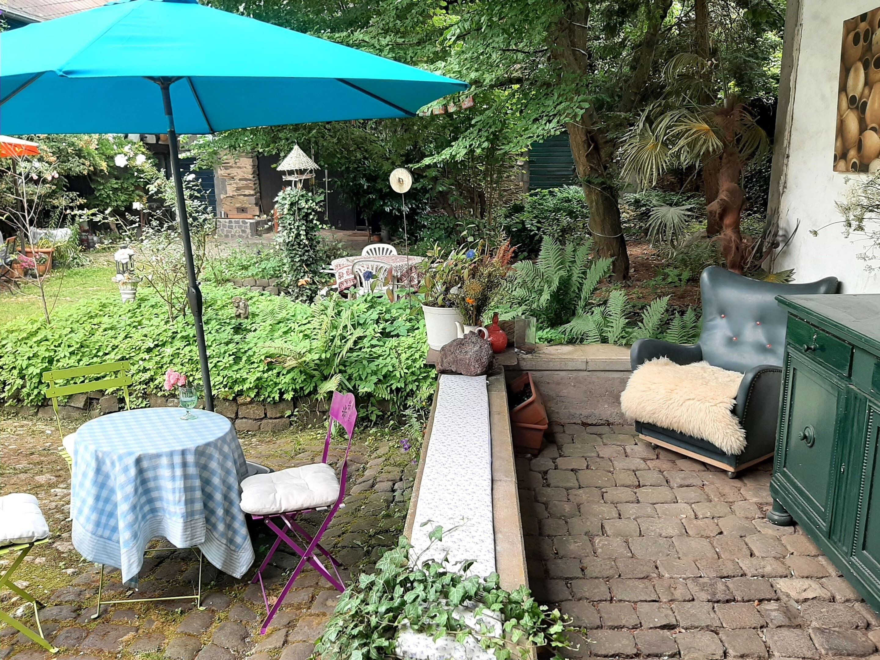 A patio area with a table and chairs, a bench, a green cabinet, and a blue umbrella.