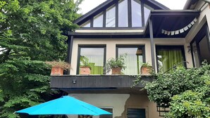 Una casa de dues plantes amb un balcó, un para-sol blau i plantes en testos.