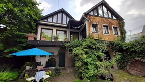 Una casa de dues plantes amb un balcó, una zona de menjador amb mobles d'exterior i un jardí.