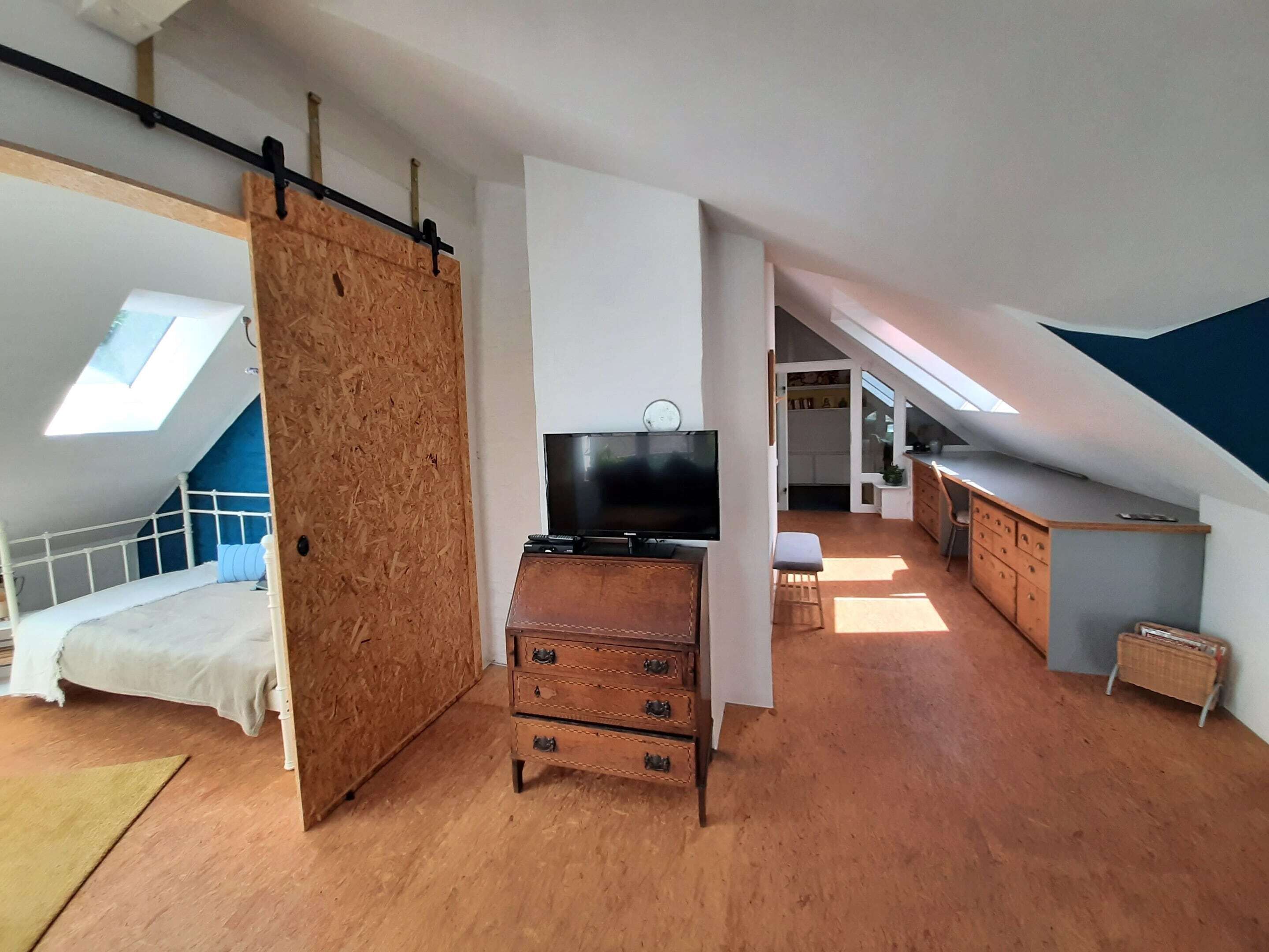 A loft-style bedroom with a bunk bed, a wooden dresser, a television, and a skylight.