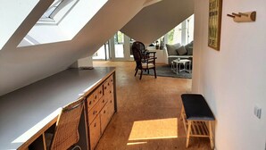 Habitació d'estil loft amb sostre inclinat, una taula de treball, una cadira, un sofà i una taula petita.