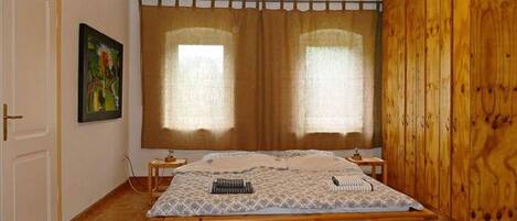 A bedroom with a wooden bed, a painting on the wall, and a window with curtains.