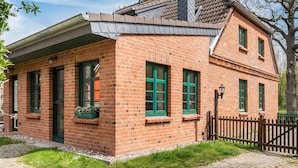 Ein Backsteinhaus mit geneigtem Dach, grünen Fensterläden und einer kleinen Veranda mit Blumentöpfen.