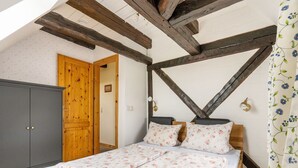 Ein Schlafzimmer mit schrägen Wänden, Holzbalken, einem Bett mit floralem Bettzeug, einem Kleiderschrank und einer Tür.