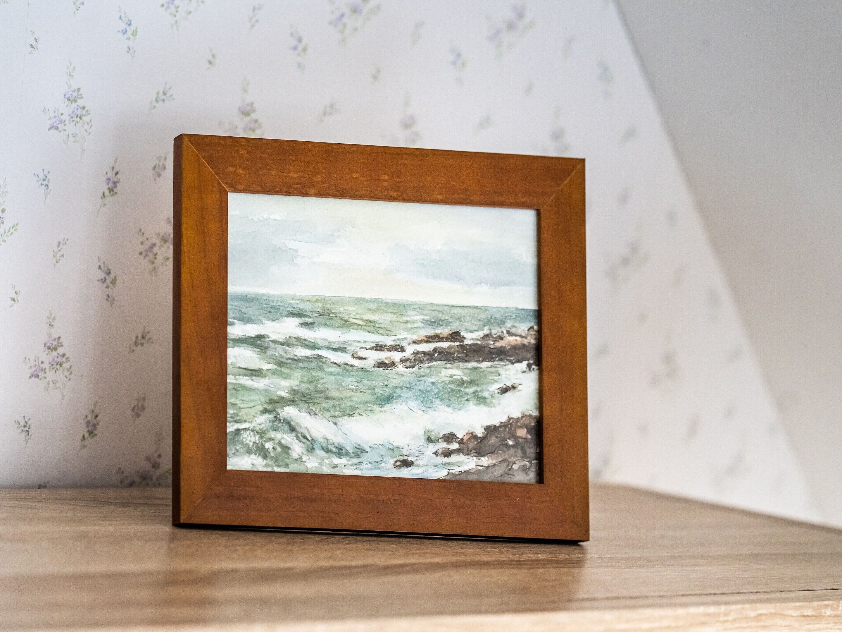 Un tableau encadré représentant un paysage marin, peint sur une surface en bois.