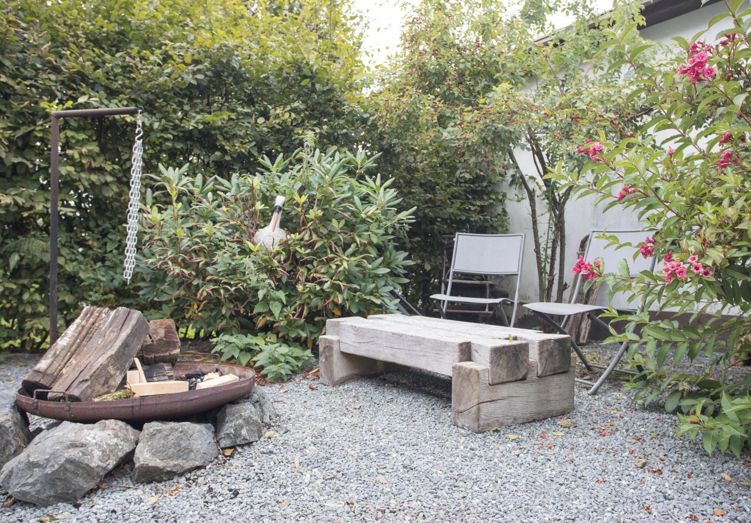 Un jardin avec un foyer, un banc en bois et une chaise en métal.