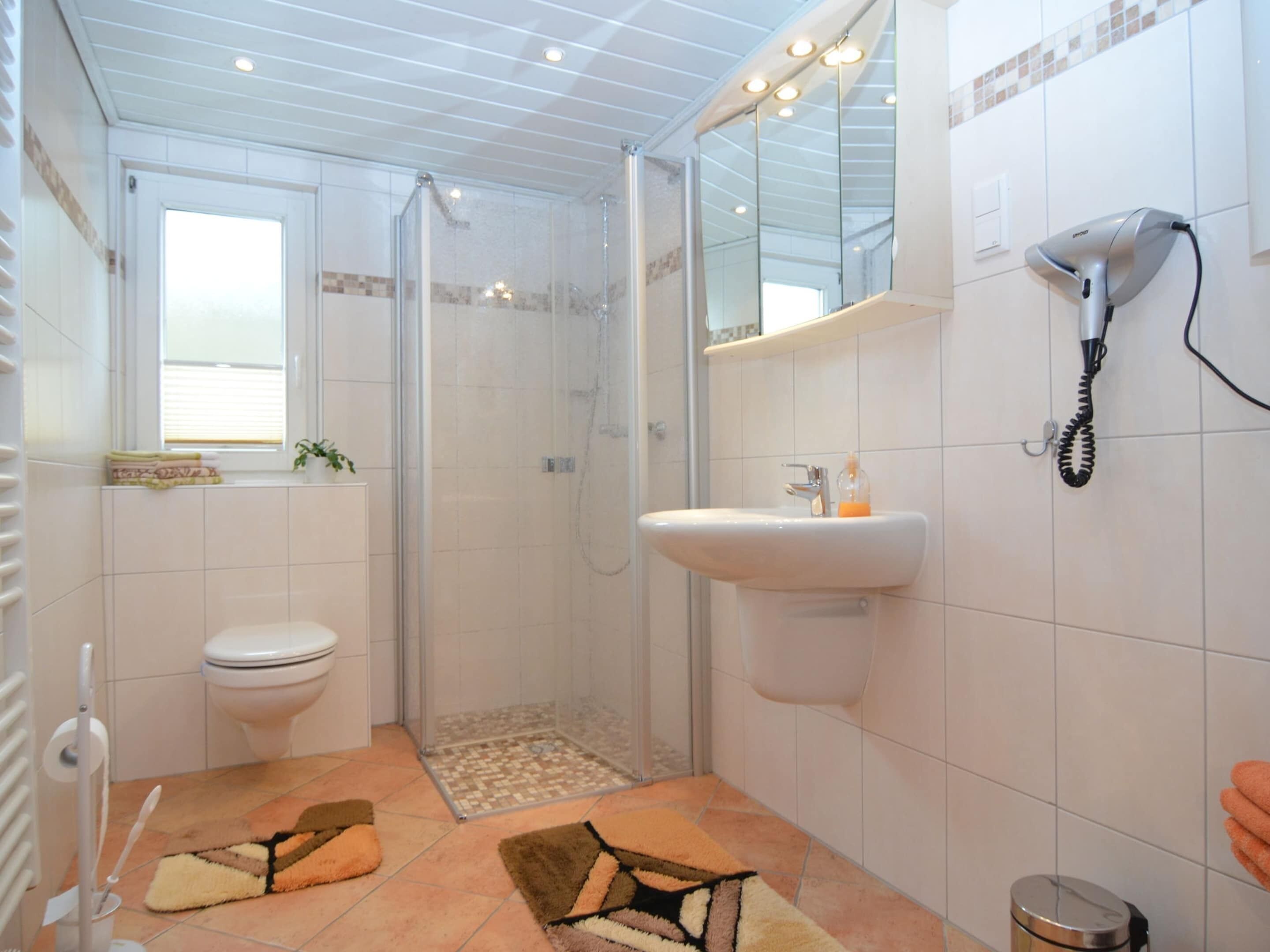 Ein Badezimmer mit Toilette, Dusche, Waschbecken und einem Haartrockner an der Wand.
