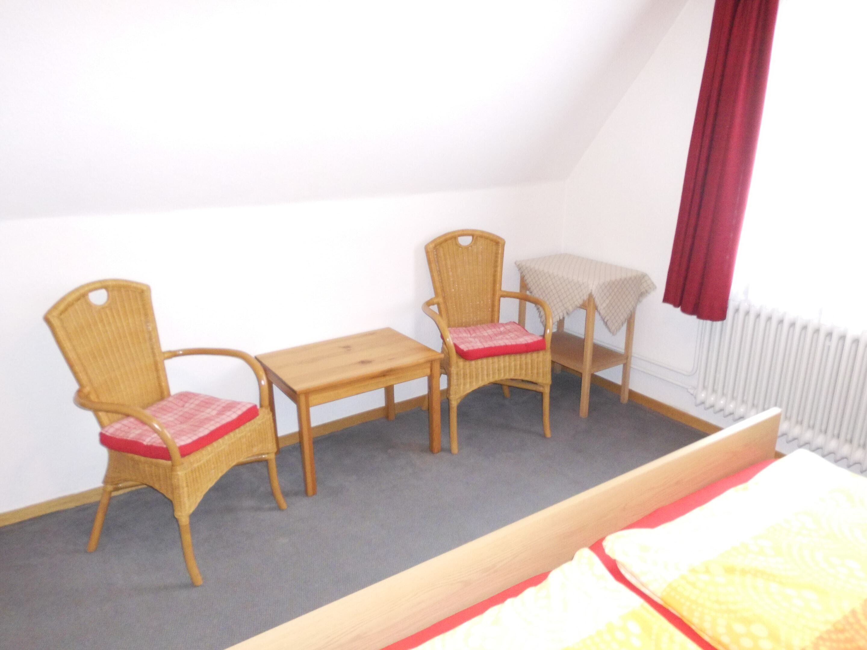 A small room with two wicker chairs, a wooden table, and a bed.
