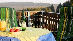 A table set with a bottle of wine, glasses, and a bowl of fruit on a balcony with a view of a forested landscape. - Apartment in Langewiese Near Winterberg (Winterberg)