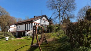 A traditional house with a sloped roof, a garden with a swing set, and a clear blue sky. - Flat in Meldorf Next to the Town Centre (Meldorf)