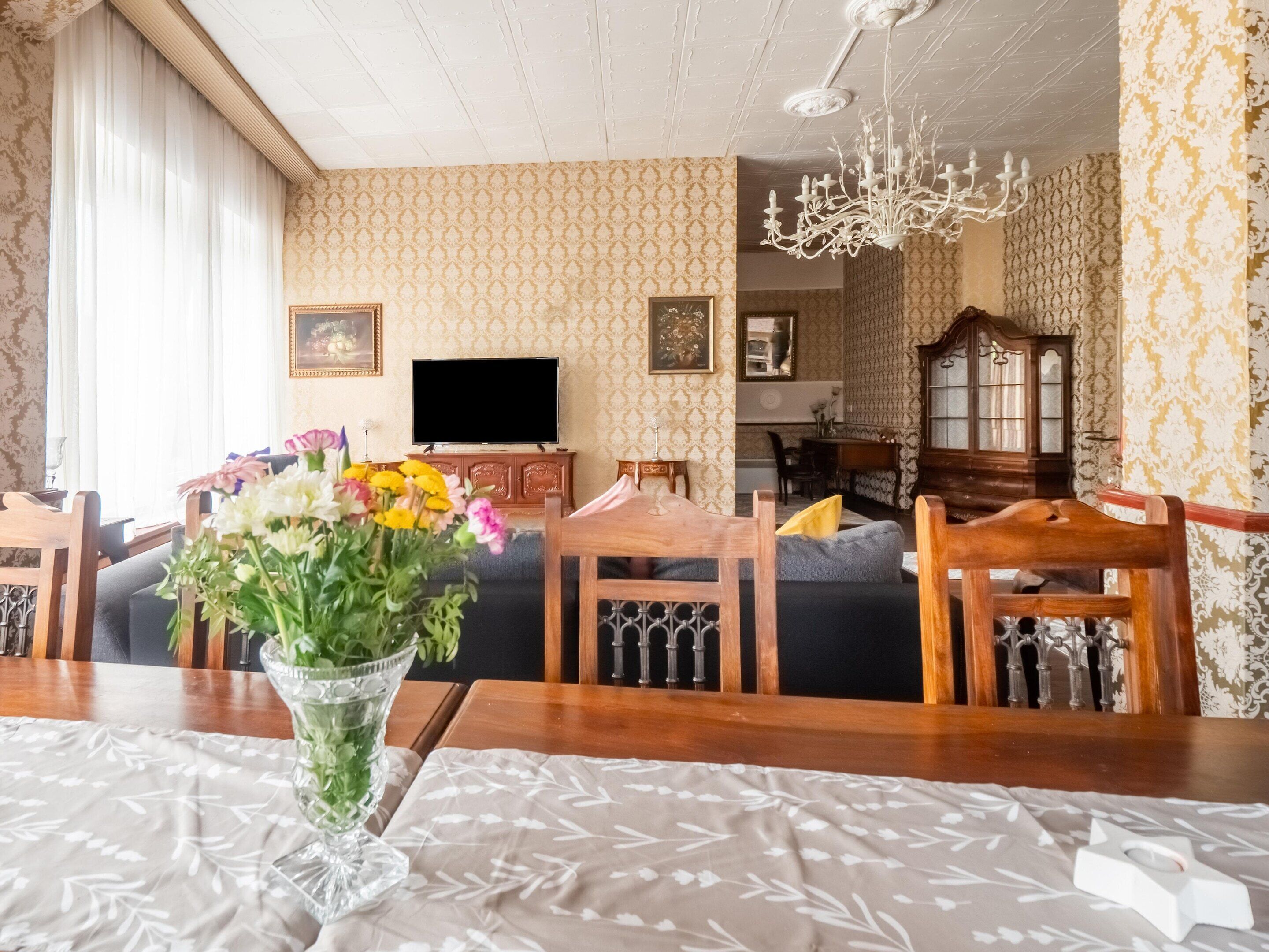 A dining area with a wooden table, chairs, a vase of flowers, and a television.