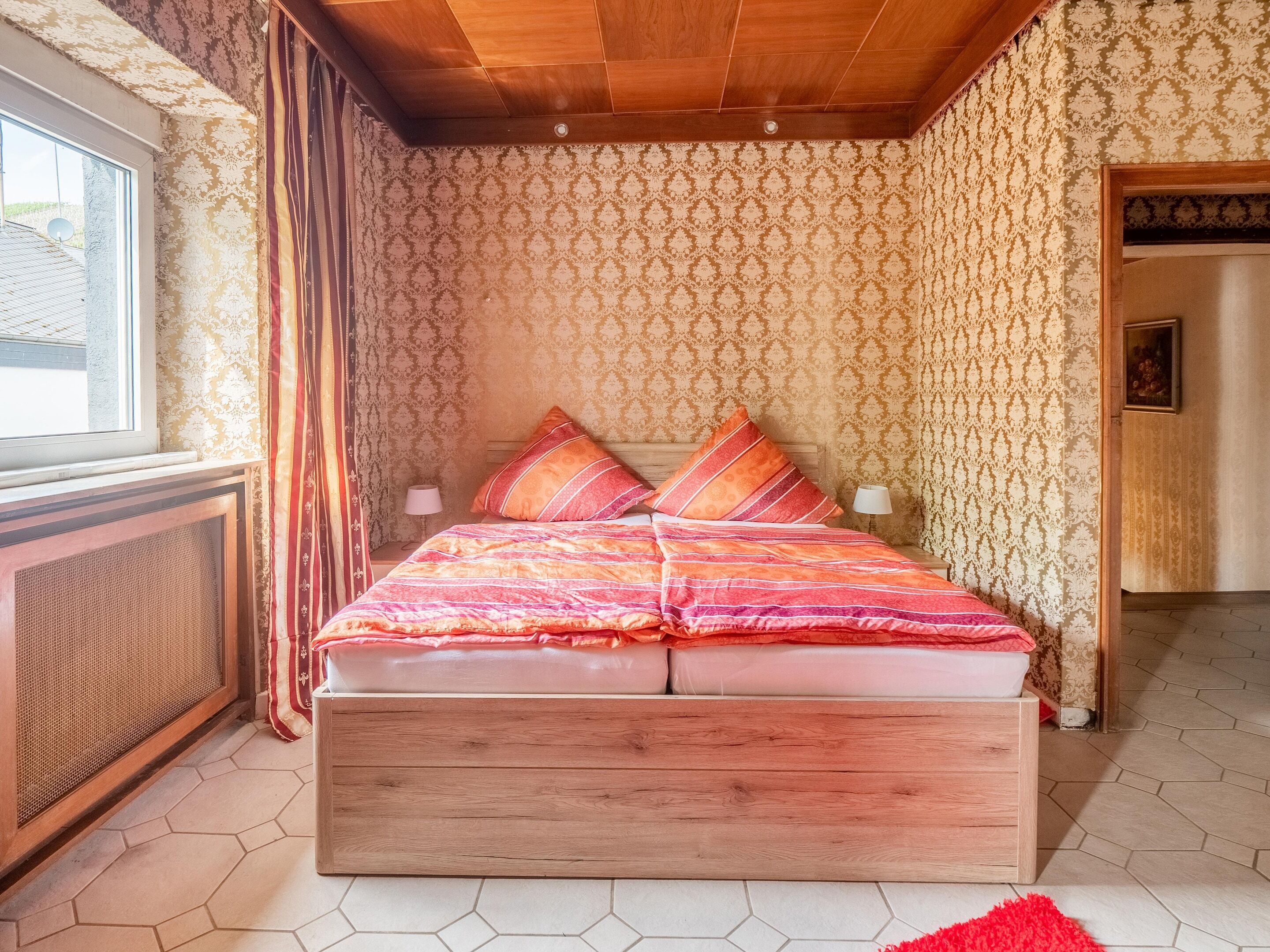 A bedroom with a wooden bed, patterned wallpaper, and a view of the outdoors.