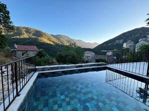 A swimming pool with a tiled deck, surrounded by stone walls and a metal railing.