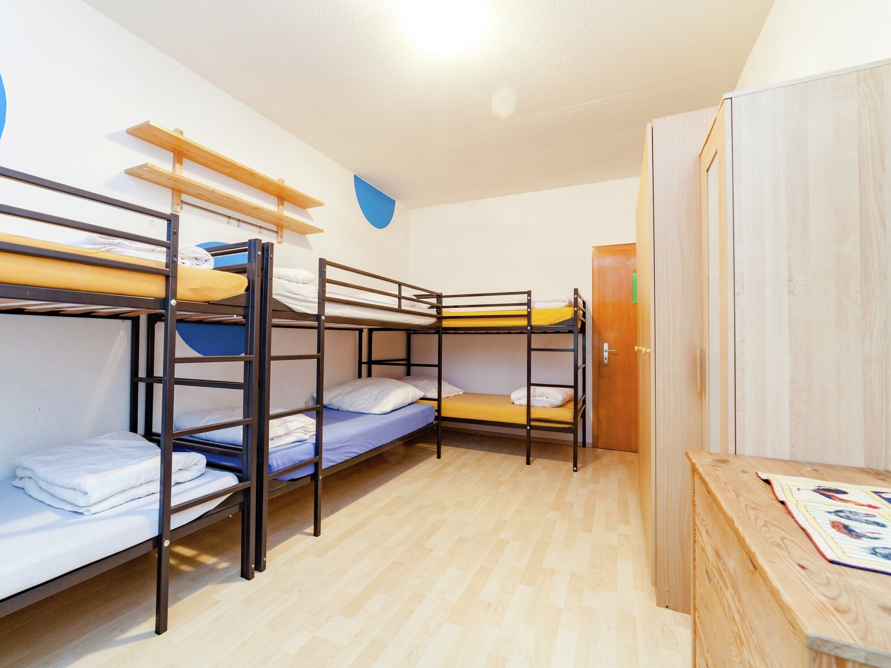 Een slaapzaal met stapelbedden, een houten bureau en een kledingkast.
