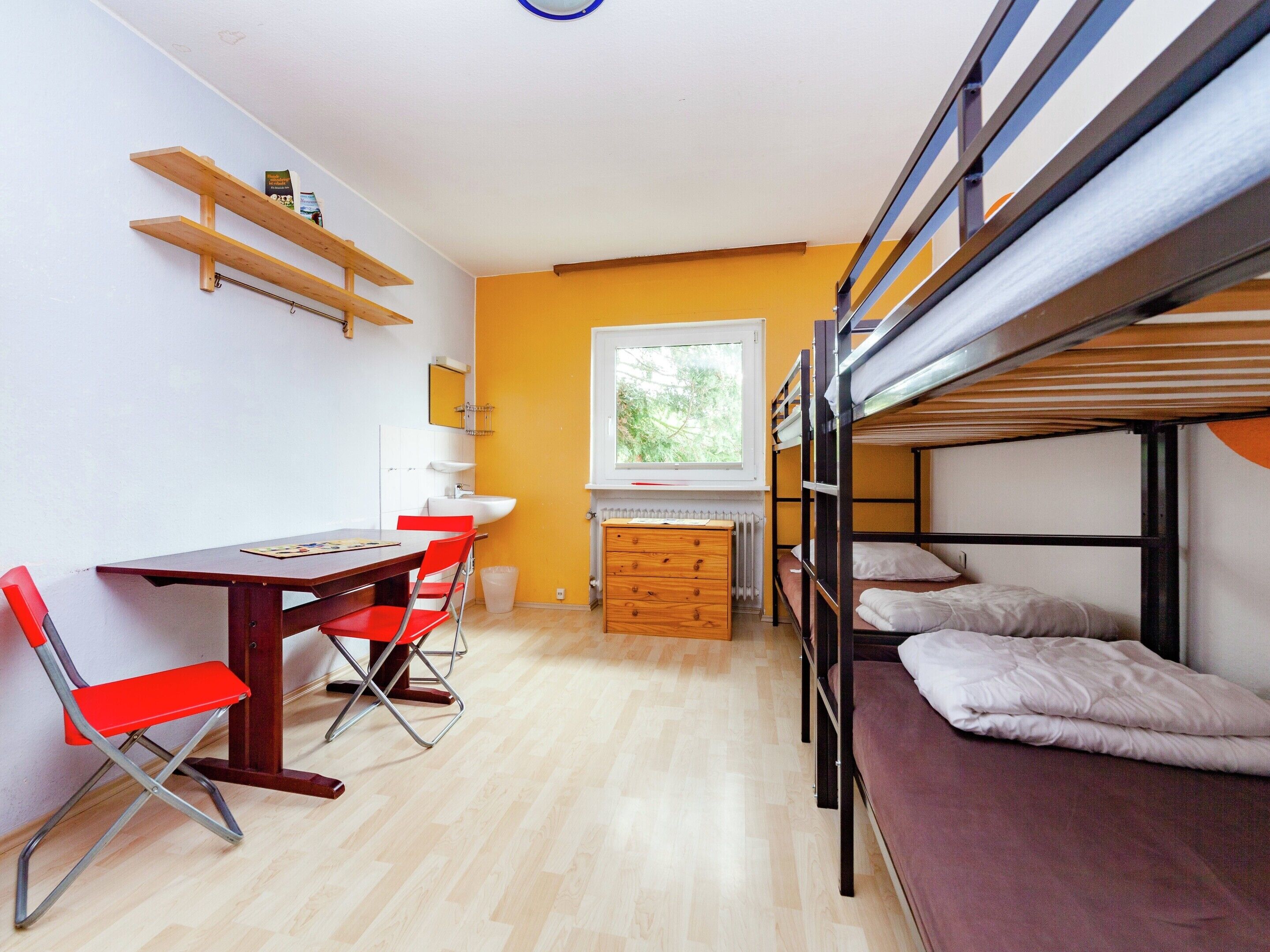 Une chambre de dortoir avec des lits superposés, un bureau avec des chaises, un radiateur et une fenêtre.