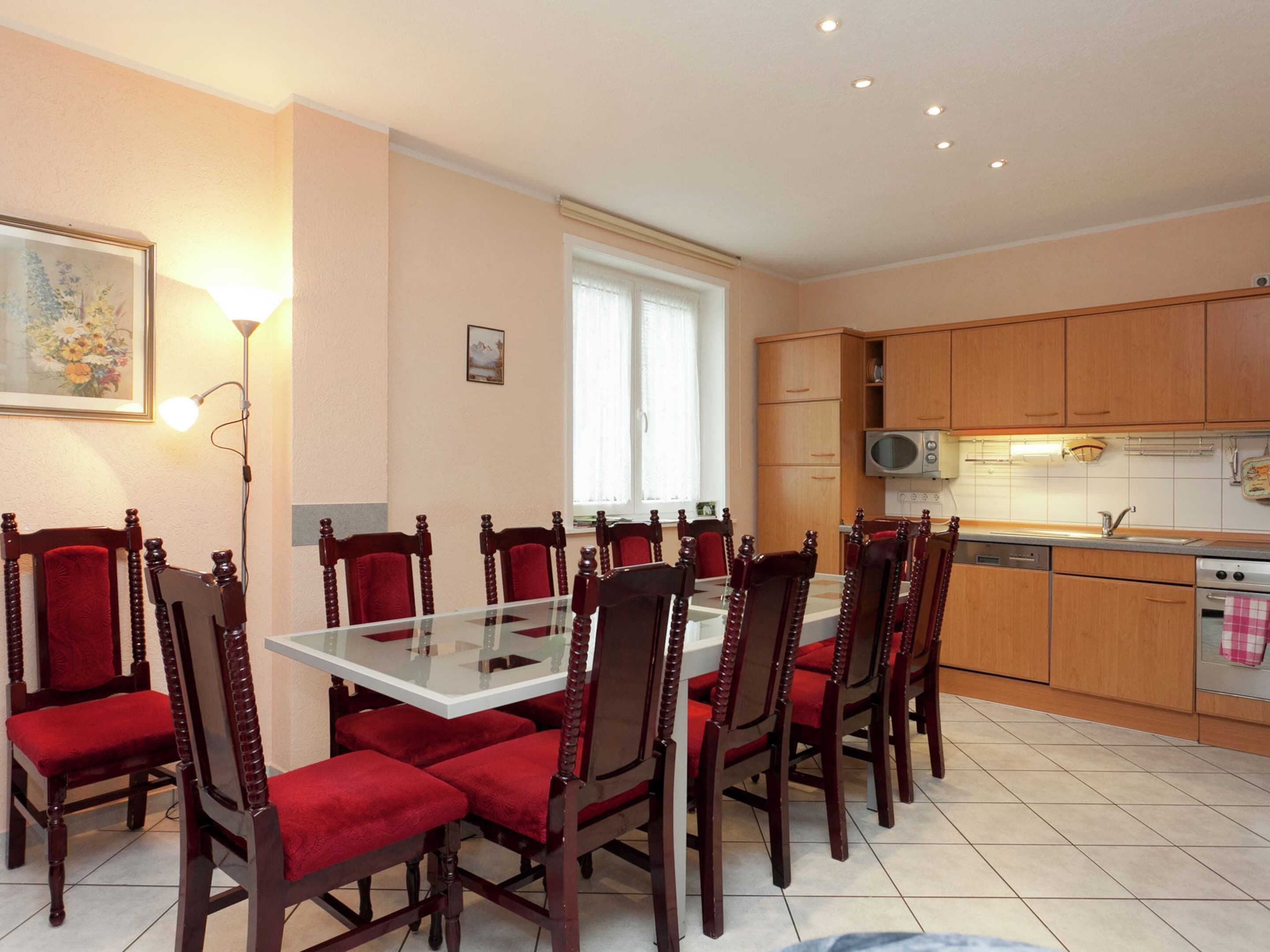 Un coin repas avec une table en verre et des chaises en bois, une cuisine avec des meubles en bois et des appareils électroménagers, et une fenêtre avec des rideaux.