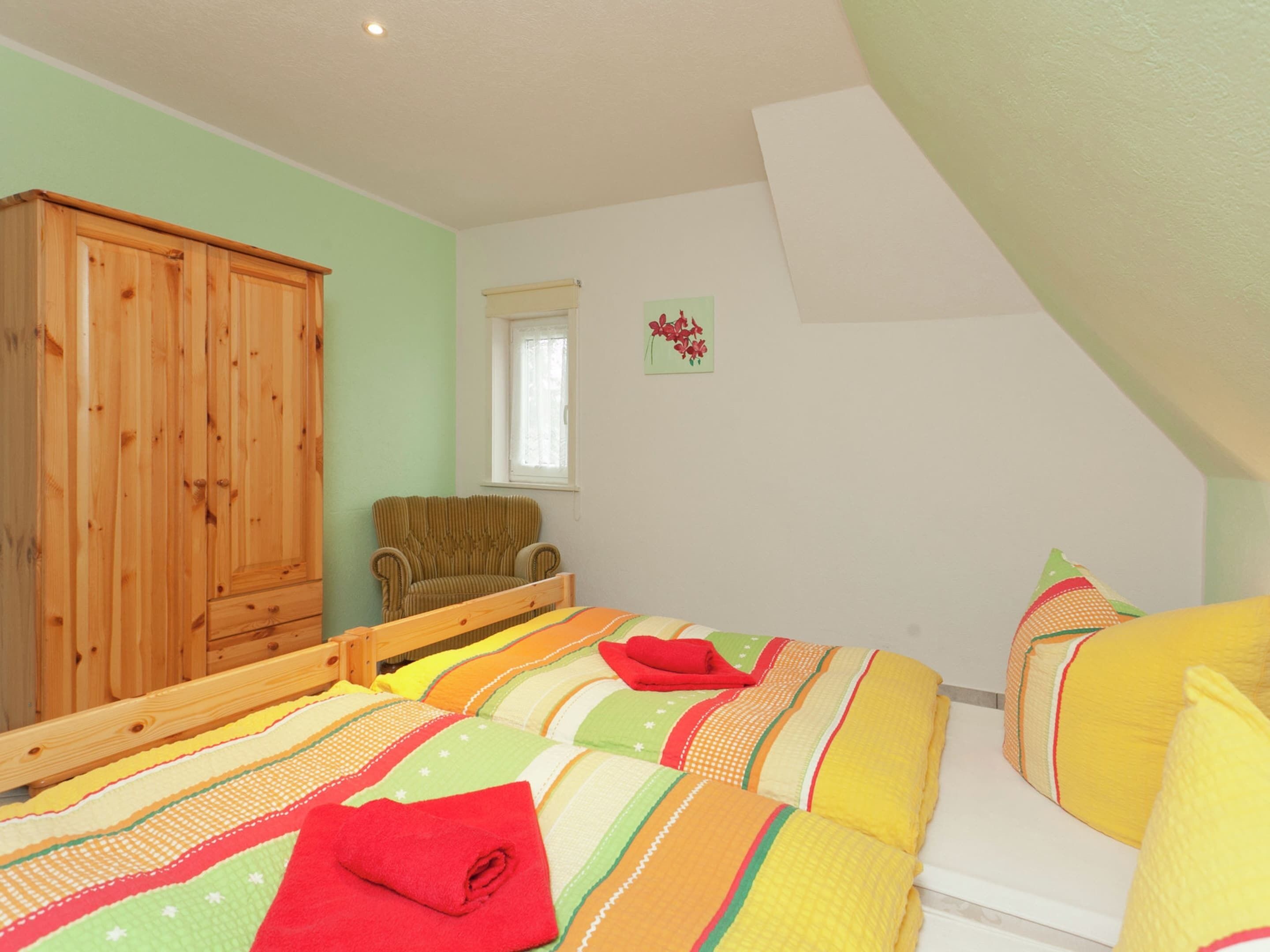 A bedroom with two beds, a wooden wardrobe, a chair, and a window.