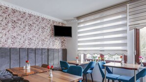 A modern restaurant with wooden tables and blue chairs, a floral wallpaper, and a large window with blinds. - Apartment in Oberhausen Near Dusseldorf (Oberhausen)