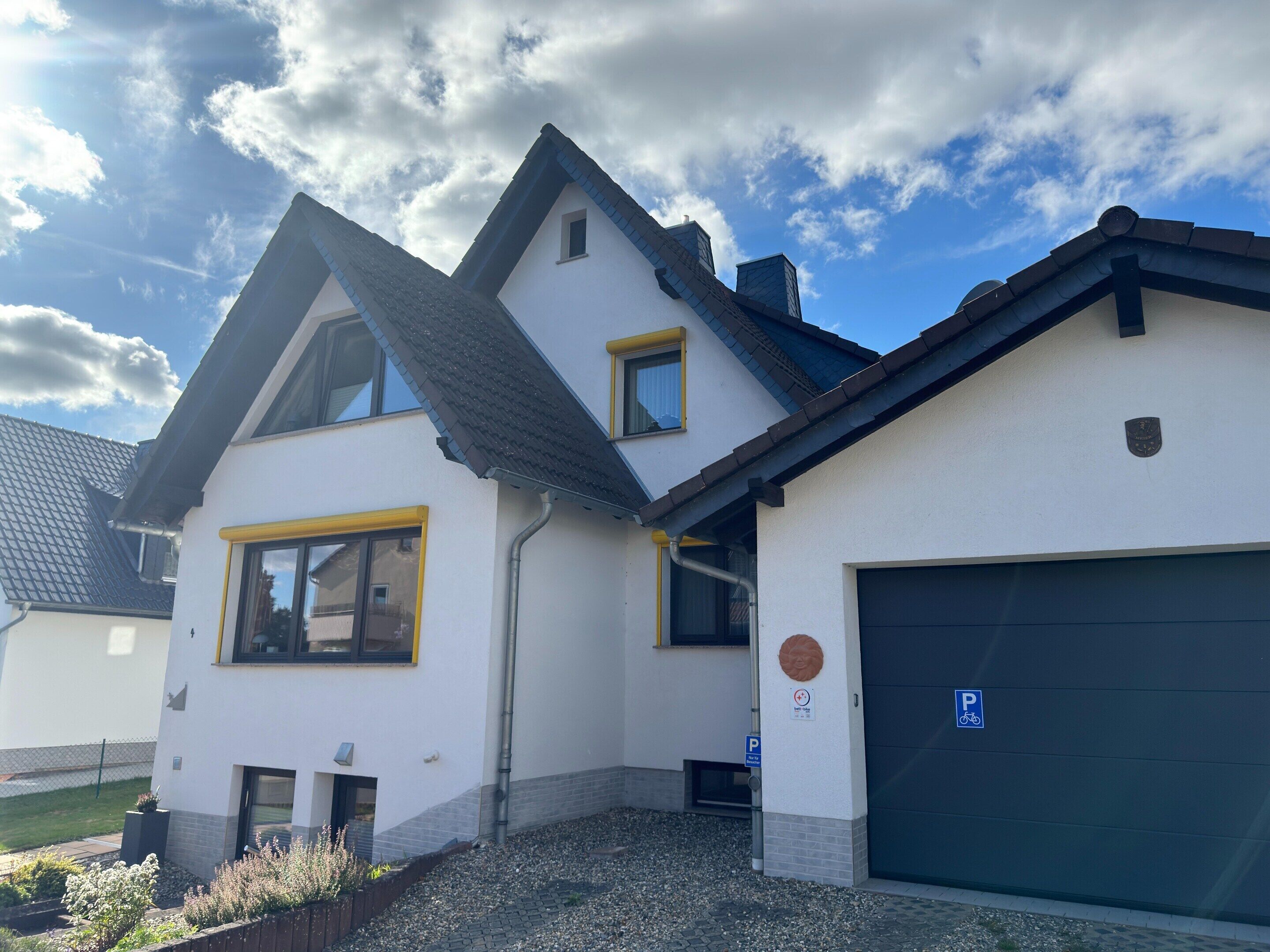 Uma casa de dois andares com garagem, entrada por automóvel e um pequeno jardim.