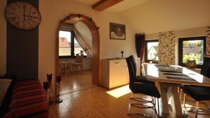 A room with a wooden floor, a dining table with chairs, a clock on the wall, and a framed picture. - Wohnung in Frankenberg fur Radfahrer (Frankenberg)