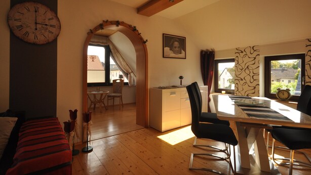 A room with a wooden floor, a dining table with chairs, a clock on the wall, and a framed picture. - Wohnung in Frankenberg fur Radfahrer (Frankenberg)