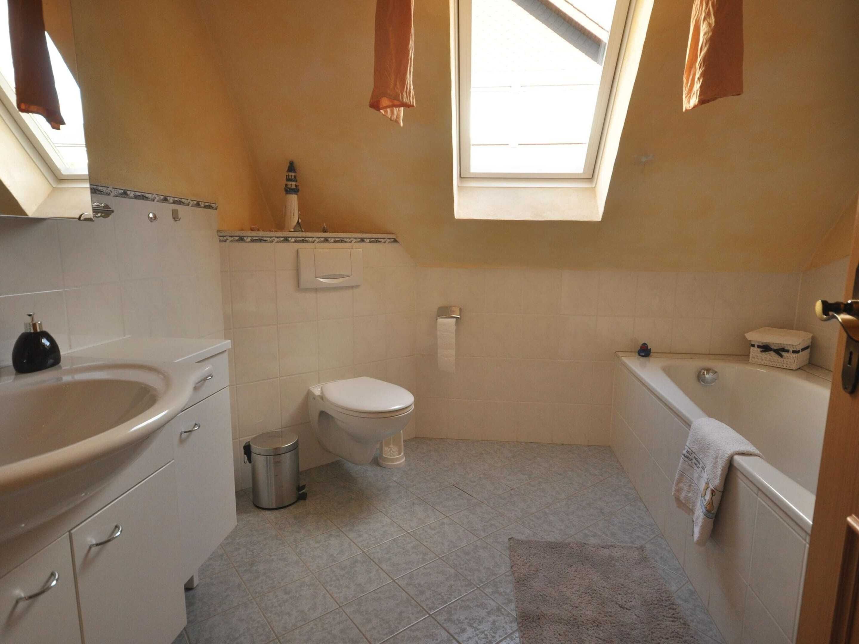 A bathroom with a toilet, sink, and bathtub. There is a skylight above the toilet and a small trash can next to the sink.