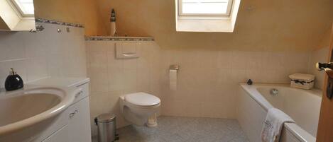 A bathroom with a toilet, sink, and bathtub. There is a skylight above the toilet and a small trash can next to the sink.