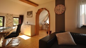 A modern living room with a black sofa, a dining table with chairs, a kitchen area, and a large wall clock. - Wohnung in Frankenberg fur Radfahrer (Frankenberg)