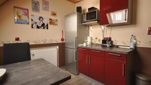 A kitchen with a refrigerator, microwave, and red cabinets. There are posters on the wall and a table with chairs. - Wohnung in Frankenberg fur Radfahrer (Frankenberg)