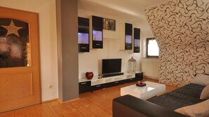 A modern living room with a wooden floor, a black sofa, a white coffee table, and a TV on a black stand. - Wohnung in Frankenberg fur Radfahrer (Frankenberg)