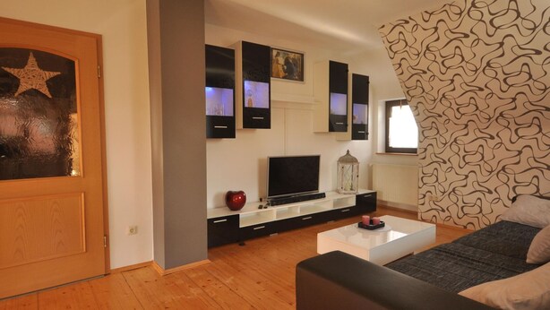 Un salon moderne avec un plancher en bois, un canapé noir, une table basse blanche et un téléviseur posé sur un meuble noir.