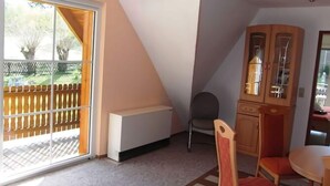 Een kamer met een schuifglasdeur die uitkomt op een terras, een houten kast, een stoel en een kleine tafel.