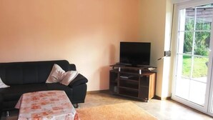 Een woonkamer met een bank, een salontafel, een tv op een standaard en een schuifdeur naar een tuin.