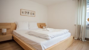 A minimalist bedroom with a wooden bed, white linens, a bedside lamp, and a framed picture on the wall. - Modernes Appartement Neben Einem Skigebiet (Winterberg)