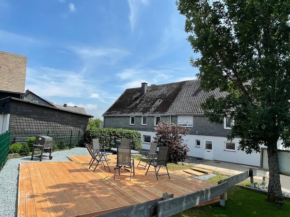Une terrasse en bois avec des meubles d’extérieur, un mur en pierre et un bâtiment doté d’un toit en pente.