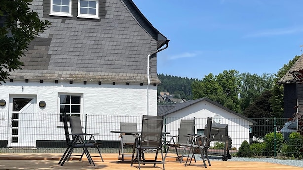 A house with a white exterior, a grey roof, and a wooden deck with outdoor furniture. - Modernes Appartement Neben Einem Skigebiet (Winterberg)