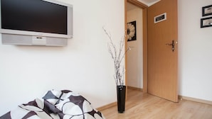 A room with a bed, a television mounted on the wall, a wooden door, and a small potted plant. - Modernes Appartement Neben Einem Skigebiet (Winterberg)
