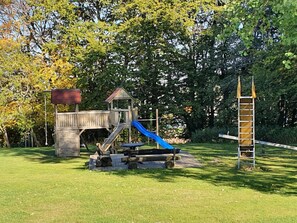 A wooden play structure with a slide and climbing area, surrounded by grass and trees. - Ferienhaus mit Terrasse im Skigebiet (Willingen)