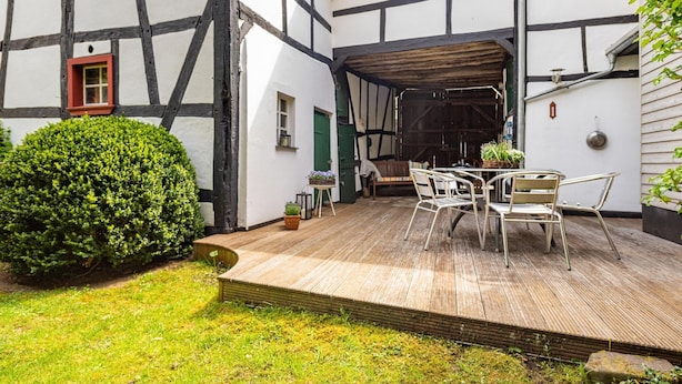 A traditional half-timbered building with a wooden deck, outdoor seating, and a green bush. - Romantic Holiday Home in Schleiden on the Village Square (Schleiden)