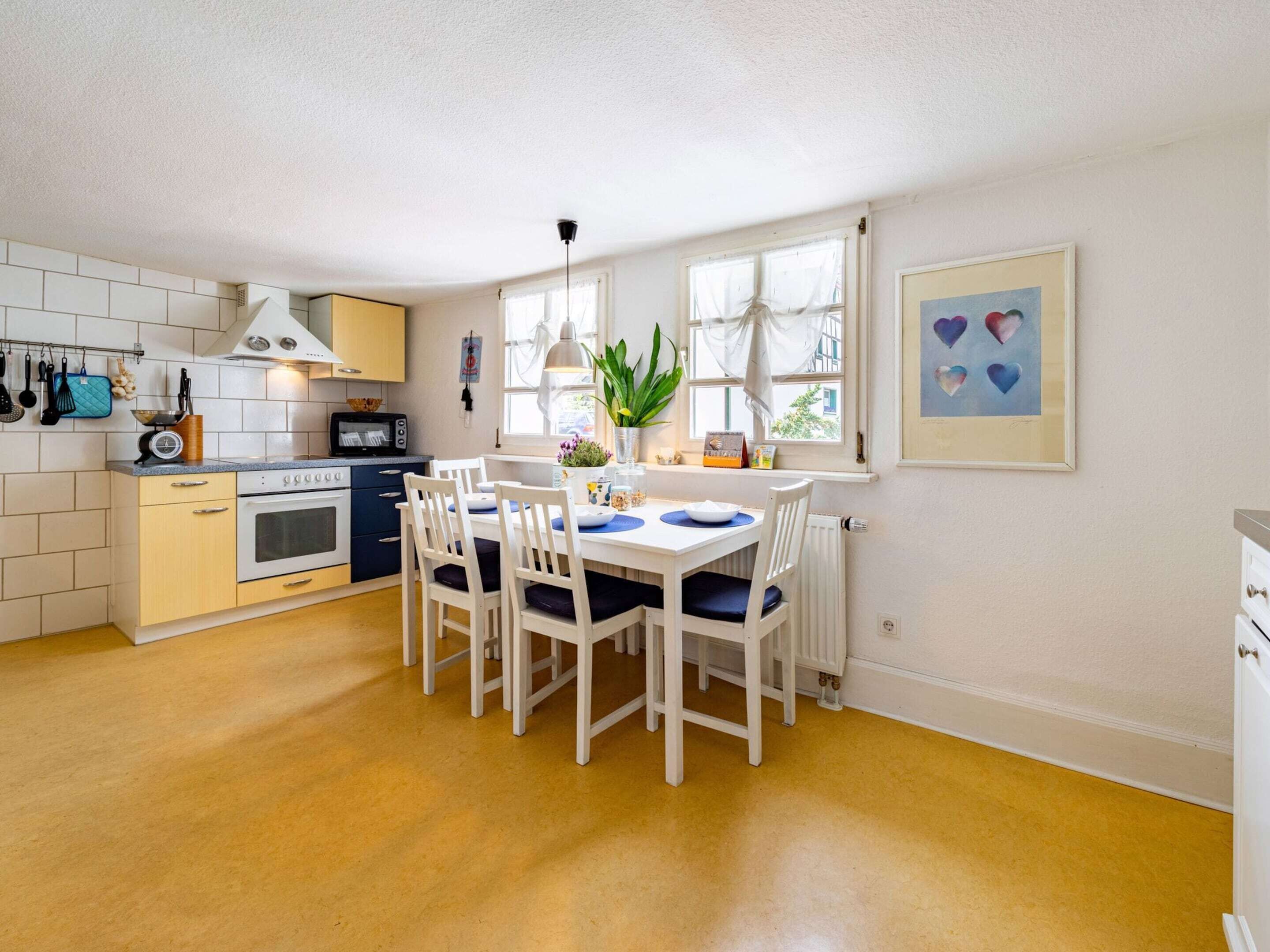 A compact kitchen with a dining area, featuring a white table, chairs, and a window with curtains.