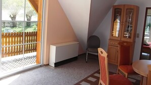 Ein Zimmer mit einer Schiebetür zum Balkon, einem Holzschrank, einem Stuhl und einem kleinen Tisch.