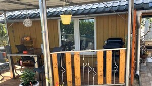 A wooden structure with a covered patio area, a table with chairs, and a potted plant with flowers. - Snug Apartment in Grevesmuhlen With Terrace (Grevesmuehlen)