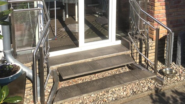 A residential building with a covered porch, a metal railing, and a small outdoor seating area. - Snug Apartment in Grevesmuhlen With Terrace (Grevesmuehlen)