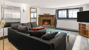 A modern living room with a black sofa, a fireplace, a flat-screen TV, and a large window. - Snug Apartment in Grevesmuhlen With Terrace (Grevesmuehlen)