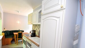 A compact kitchen with white cabinetry, a coffee maker, and a dining area with a green sofa and wooden table. - Bungalow in the Harz Mountains With Terrace (Oberharz am Brocken)