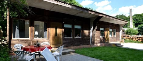 Een houten hut met een patio, inclusief een tafel en stoelen, en een overdekte zitplek buiten.