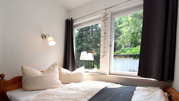 A neatly made bed with white and dark gray bedding, a wooden headboard, and a window with curtains. - Bungalow in the Harz Mountains With Terrace (Oberharz am Brocken)